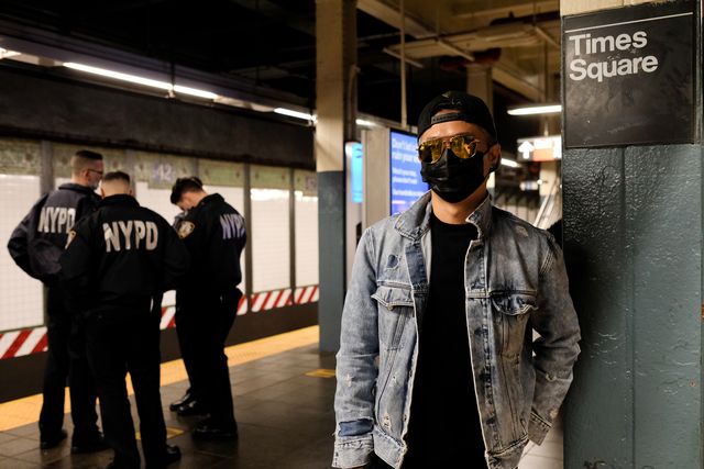 A man poses for a photo in a subway station. Three police officers stand in the background.